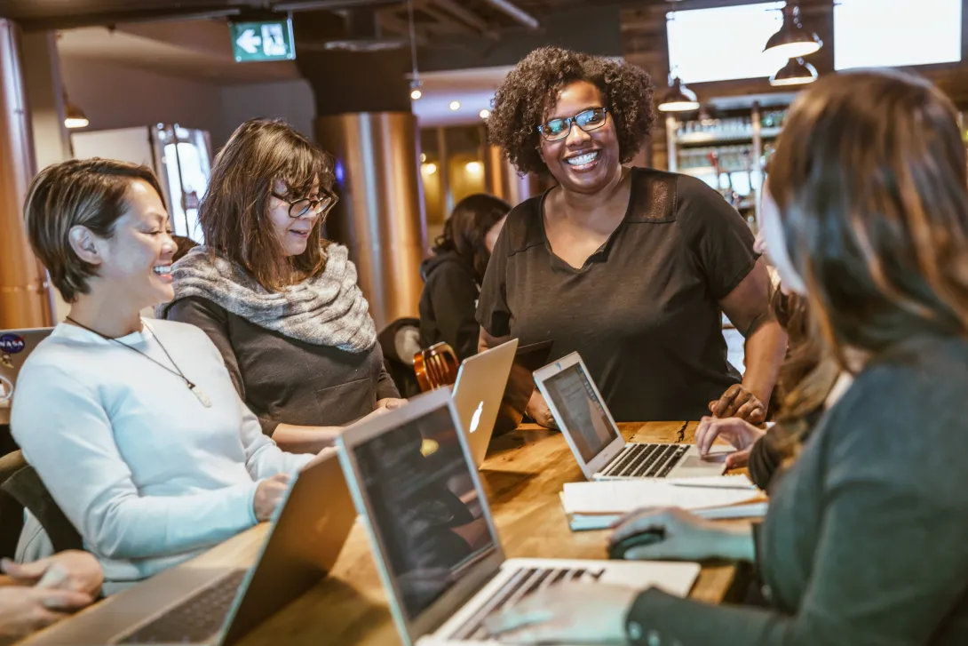 Smiling people at an office table working on laptops