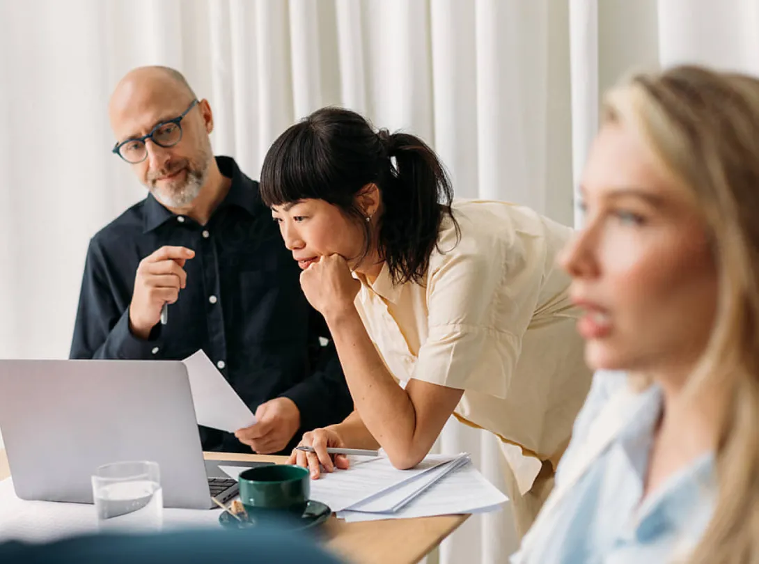 Two people in background reviewing laptop one person speaking in forground