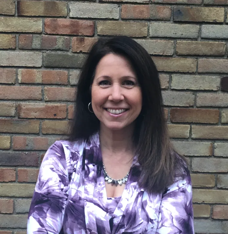 Lori smiling in front of a brick wall